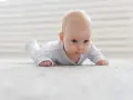 Niemowlę na brzuchu cofa ręce do tyłu, ćwicząc mięśnie.