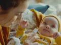 Mama sprawdza, czy niemowlaka nie dopadła gorączka. Dziecko w żółtym ubranku patrzy z zaciekawieniem na termometr.