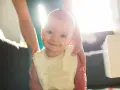 Uśmiechnięte niemowlę wkłada rączki do ust i się ślini, ubrana w śliniaczek.