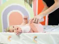 Niemowlę ćwiczy obręcz barkową. Mama delikatnie podnosi nóżki dziecka, wspierając jego rozwój.