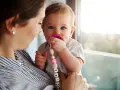 Maluch karmiony piersią z niebieskimi oczami ssie różowy smoczek. Mama trzyma go na rękach, a smoczek ma zawieszkę z imieniem.