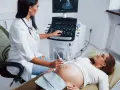 Lekarka wykonuje USG ciężarnej. Na ekranie widoczny obraz płodu, który będzie porównany z siatką centylową płodu tabela.