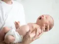 Niemowlę ziewające w ramionach taty. Jedno oko jest lekko przymknięte, drugie otwarte, jakby chciało zobaczyć świat.