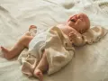 Płaczące, dwuletnie dziecko się pręży i napina, leżąc na jasnym kocyku.