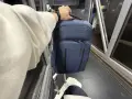 Ręka trzyma granatowy plecak, idealny na podróż z Ryanair. Obok walizka i rękaw lotniska.