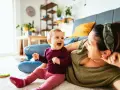 Radosne dziecko 7 miesięcy śmieje się do mamy, leżąc na dywanie.