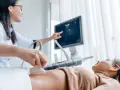 Lekarka wykonuje badania prenatalne 1 trymestr, przykładając głowicę USG do brzucha pacjentki. Na ekranie widoczny obraz.