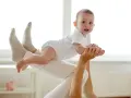 Radość z zabaw z 6 miesięcznym dzieckiem. Maluch w białym body unosi się w powietrzu, trzymany przez rodzica.