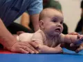 Niemowlę na brzuchu, z rękami podtrzymującymi jego tułów. Widoczna asymetria u niemowlaka podczas ćwiczeń.