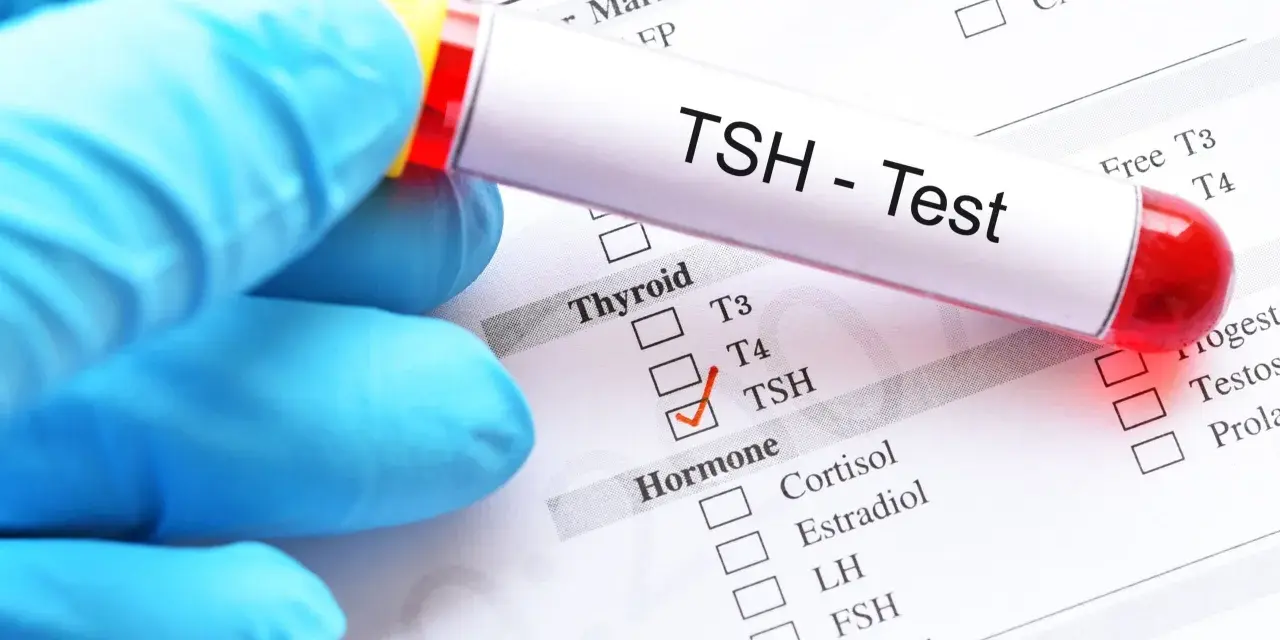 Ręka w niebieskiej rękawiczce trzyma probówkę z napisem "TSH - Test". Na papierze zaznaczono TSH, co może oznaczać badanie w ciąży.