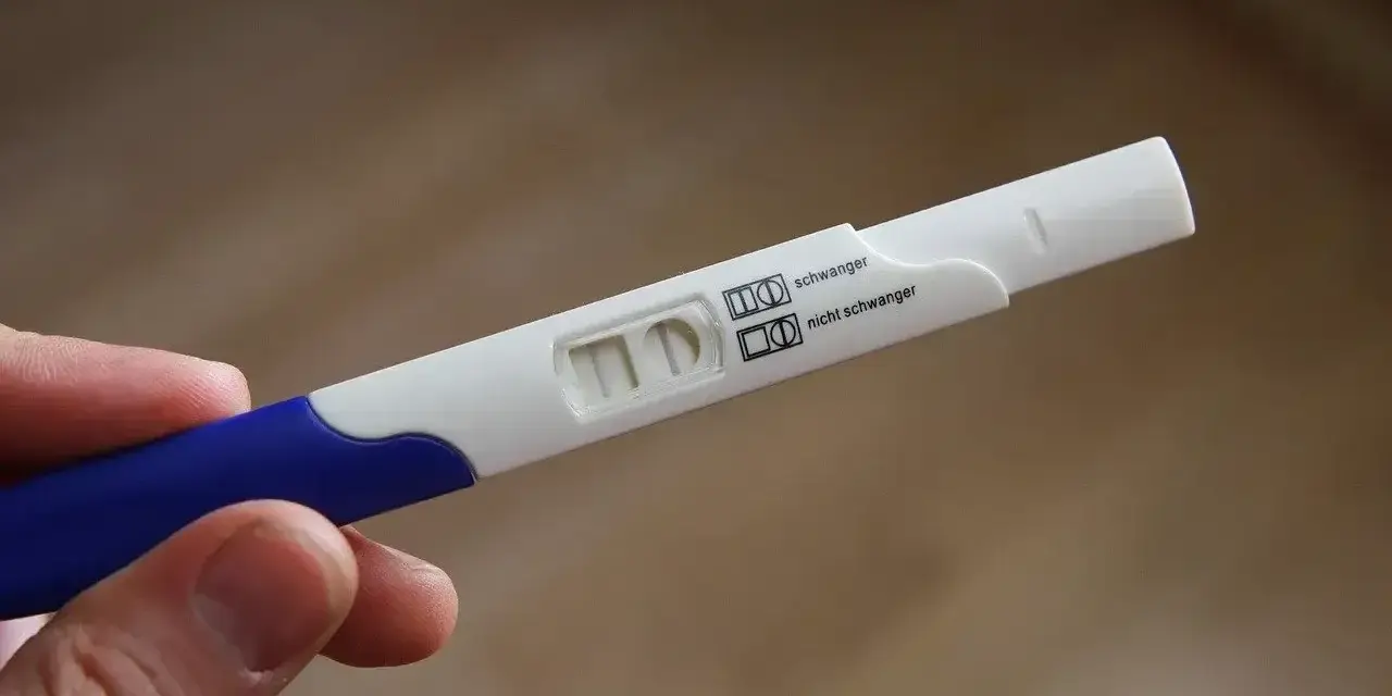 Test ciążowy w dłoni, widoczne dwa paski kontrolne. Wynik: brak okresu, test negatywny.