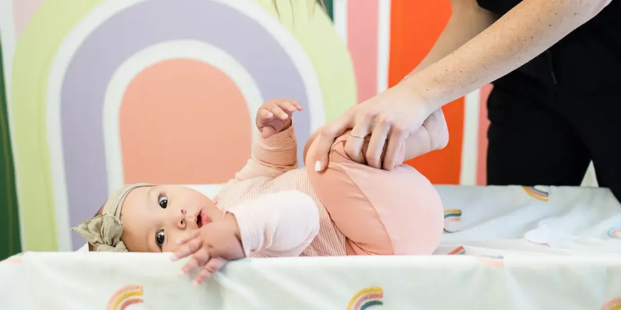 Niemowlę ćwiczy obręcz barkową. Mama delikatnie podnosi nóżki dziecka, wspierając jego rozwój.