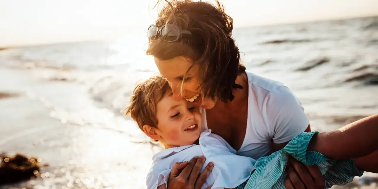 Mama tuli synka na ręce na plaży. To piękny dzień, idealny, by zaplanować wspólne chwile.