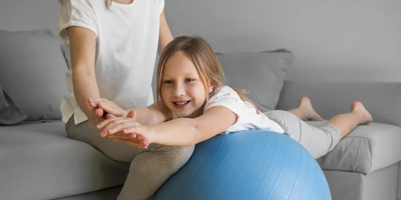 Dziecko z obniżonym napięciem mięśniowym ćwiczy chodzenie na piłce rehabilitacyjnej z pomocą terapeuty.
