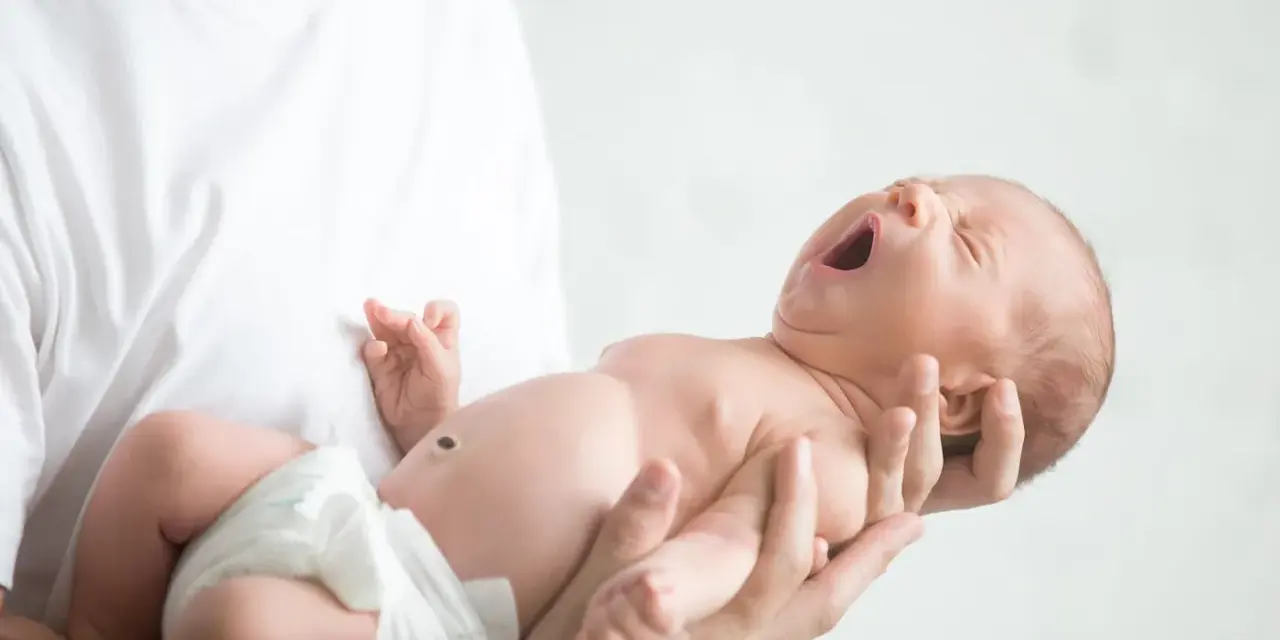 Niemowlę ziewające w ramionach taty. Jedno oko jest lekko przymknięte, drugie otwarte, jakby chciało zobaczyć świat.