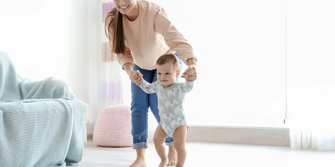 Uśmiechnięta mama pomaga dziecku stawiać pierwsze kroki. Pokazuje, jak trzymać dziecko przy nauce chodzenia, wspierając je za rączki.