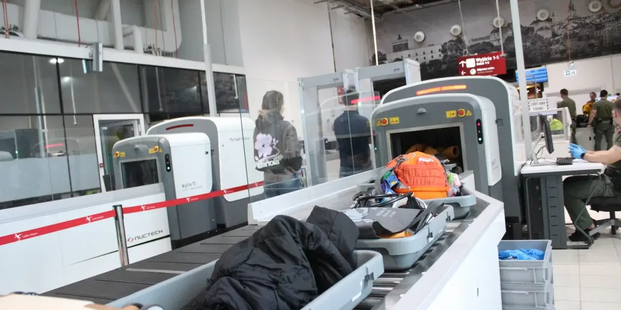 Kontrola paszportowa na lotnisku. Bagaże przechodzą przez skaner, a podróżni czekają na swoją kolej.