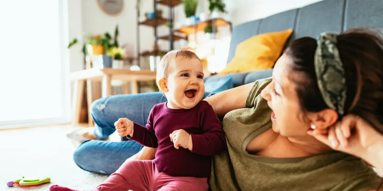 Radosne dziecko 7 miesięcy śmieje się do mamy, leżąc na dywanie.