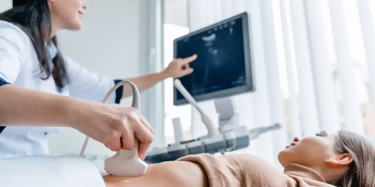 Lekarka wykonuje badania prenatalne 1 trymestr, przykładając głowicę USG do brzucha pacjentki. Na ekranie widoczny obraz.