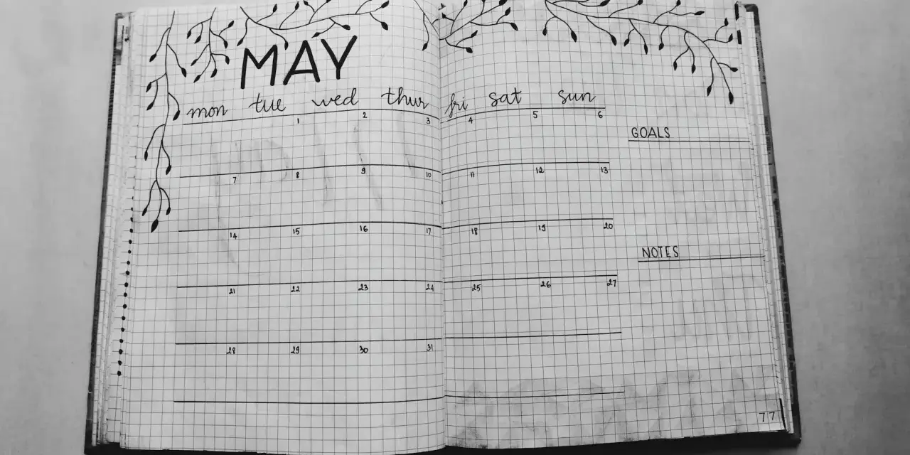 Otwarty notatnik z kalendarzem na maj, ozdobiony gałązkami. Idealny do planowania i nauki, jak prowadzić bullet journal.