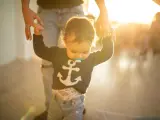 Pierwsze kroki dziecka, trzymanego za rękę. Słońce rozświetla radosny moment, kiedy dziecko zaczyna chodzić.