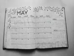 Otwarty notatnik z kalendarzem na maj, ozdobiony gałązkami. Idealny do planowania i nauki, jak prowadzić bullet journal.
