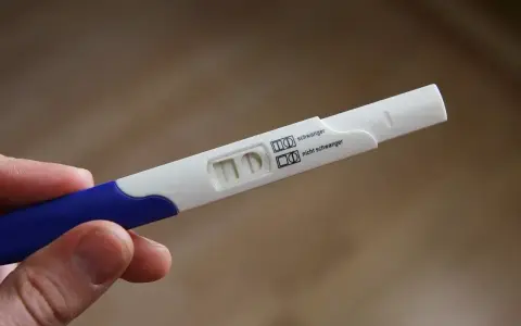 Test ciążowy w dłoni, widoczne dwa paski kontrolne. Wynik: brak okresu, test negatywny.