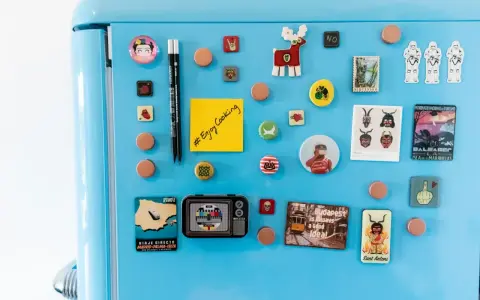 Niebieska lodówka ozdobiona magnesami: Frida Kahlo, renifer, szturmowcy, pocztówka z Madrytu, telewizor, budapeszteński tramwaj i notatnik do druku.