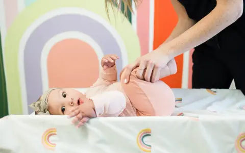 Niemowlę ćwiczy obręcz barkową. Mama delikatnie podnosi nóżki dziecka, wspierając jego rozwój.