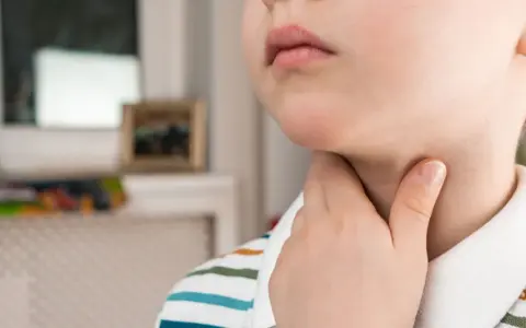 Dziecko dotyka gardła, co może być objawem bólu gardła przy covid u dzieci.