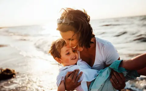 Mama tuli synka na ręce na plaży. To piękny dzień, idealny, by zaplanować wspólne chwile.
