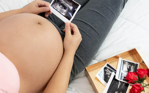 Brzuch w 10 tygodniu ciąży, z USG w dłoniach. Obok pudełko z kolejnymi zdjęciami i czerwonymi różami.