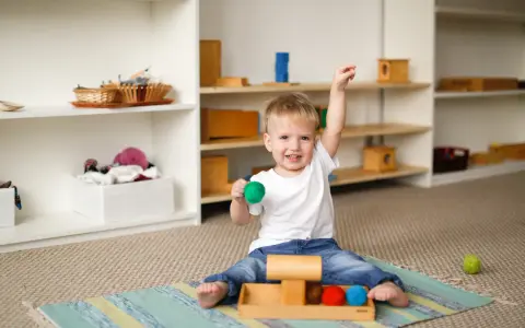 Uśmiechnięty dwulatek bawi się kolorowymi kulkami, co powinno umieć 2 letnie dziecko.
