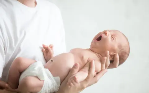 Niemowlę ziewające w ramionach taty. Jedno oko jest lekko przymknięte, drugie otwarte, jakby chciało zobaczyć świat.