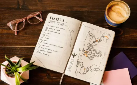 Otwarty planer podróży z listą miejsc do odwiedzenia i mapą świata. Kawa i okulary dopełniają inspirującą scenę.