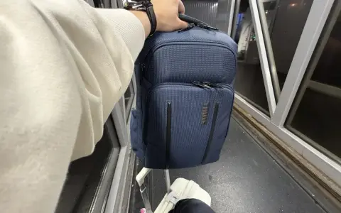 Ręka trzyma granatowy plecak, idealny na podróż z Ryanair. Obok walizka i rękaw lotniska.