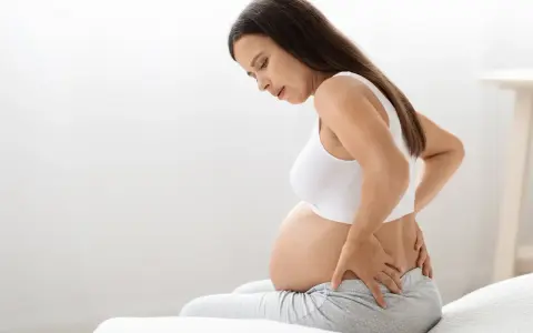 Kobieta w 38 tygodniu ciąży z bólem pleców, trzymająca się za lędźwie.