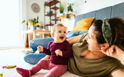 Radosne dziecko 7 miesięcy śmieje się do mamy, leżąc na dywanie.