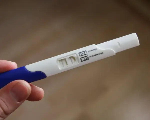 Test ciążowy w dłoni, widoczne dwa paski kontrolne. Wynik: brak okresu, test negatywny.