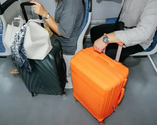 Podróżni z bagażami, w tym pomarańczową walizką, przygotowują się do lotu. Nadbagaż lot.