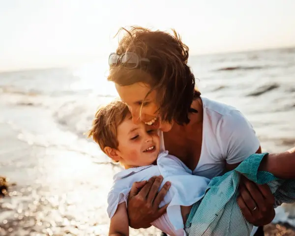 Mama tuli synka na ręce na plaży. To piękny dzień, idealny, by zaplanować wspólne chwile.