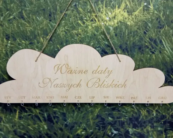 Drewniany kalendarz w kształcie chmurki z napisem "Ważne daty Naszych Bliskich". Poniżej miesiące od STY do GRU, z kółeczkami do zawieszania pamiątek. Idealny do zaznaczania każdego dnia urodzenia.