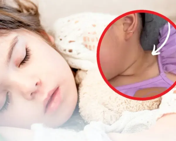 Śpiące dziecko, uśmiechnięte, z delikatnie schowaną szyją u niemowlaka pod kołderką.