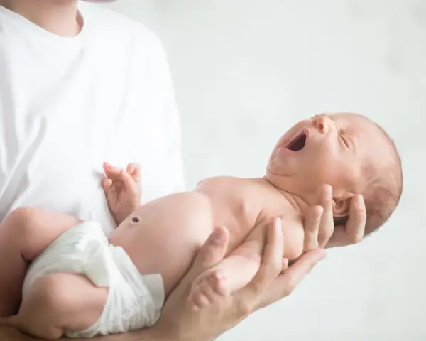 Niemowlę ziewające w ramionach taty. Jedno oko jest lekko przymknięte, drugie otwarte, jakby chciało zobaczyć świat.