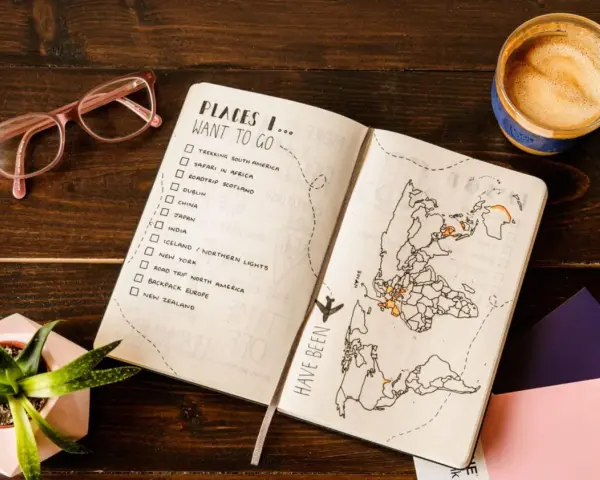 Otwarty planer podróży z listą miejsc do odwiedzenia i mapą świata. Kawa i okulary dopełniają inspirującą scenę.