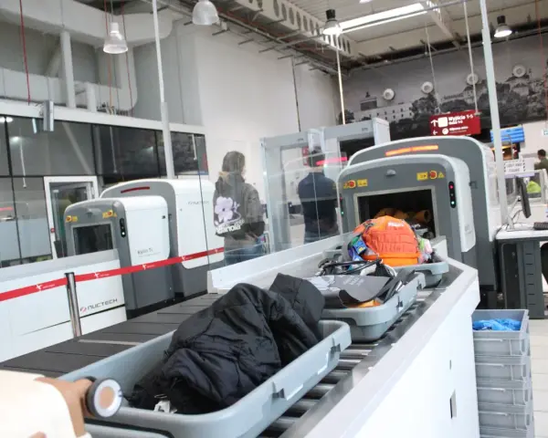 Kontrola paszportowa na lotnisku. Bagaże przechodzą przez skaner, a podróżni czekają na swoją kolej.