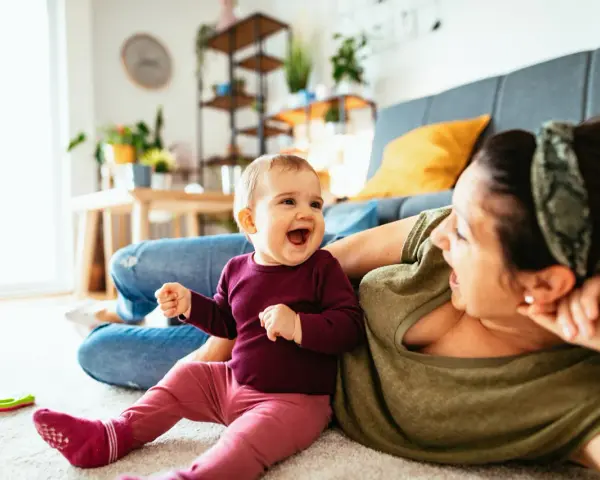 Radosne dziecko 7 miesięcy śmieje się do mamy, leżąc na dywanie.