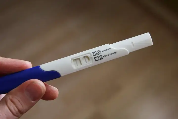 Test ciążowy w dłoni, widoczne dwa paski kontrolne. Wynik: brak okresu, test negatywny.
