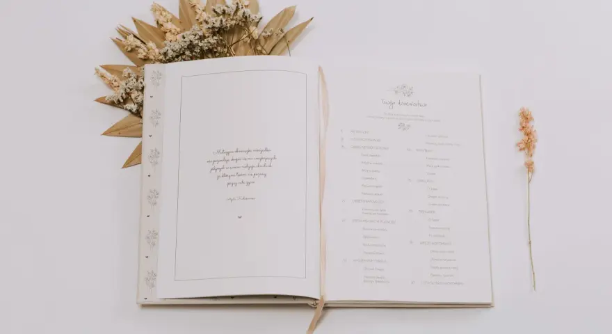 Otwarta księga z motywami roślinnymi, idealna na pierwszy album dziecka. Zawiera spis treści z rozdziałami takimi jak "Metryczka", "Roczniak" i "Dwulatek".
