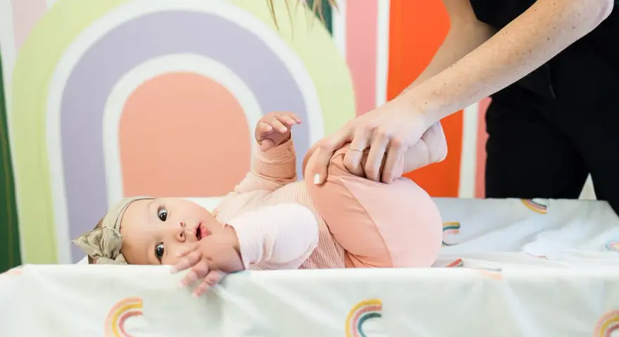 Niemowlę ćwiczy obręcz barkową. Mama delikatnie podnosi nóżki dziecka, wspierając jego rozwój.